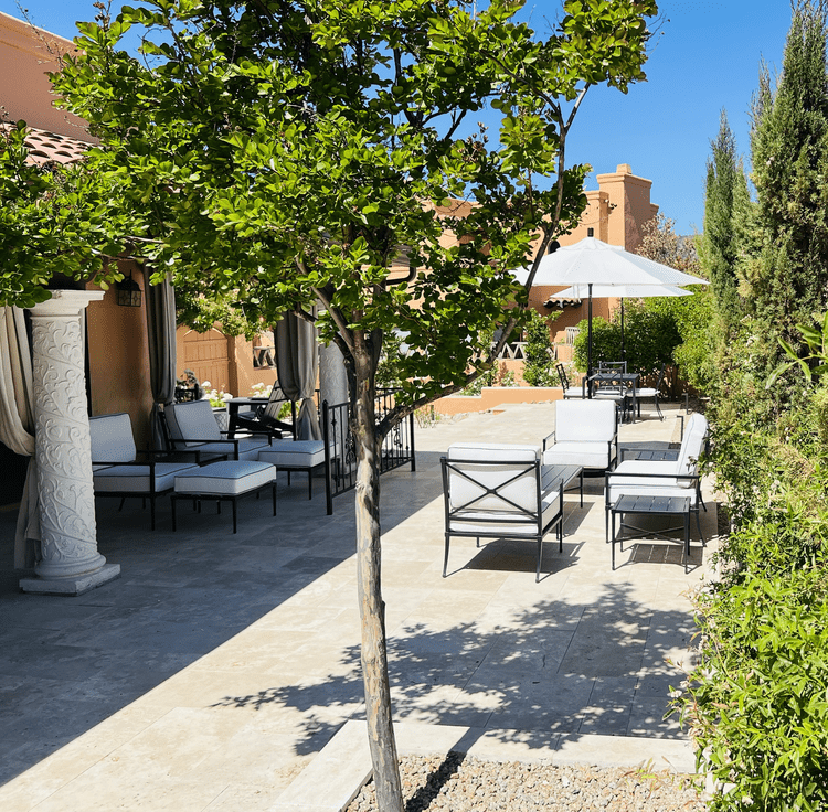 Adobe estate courtyard with ornate white columns, iron furniture, travertine pavers, and Italian cypress — Valley Estates