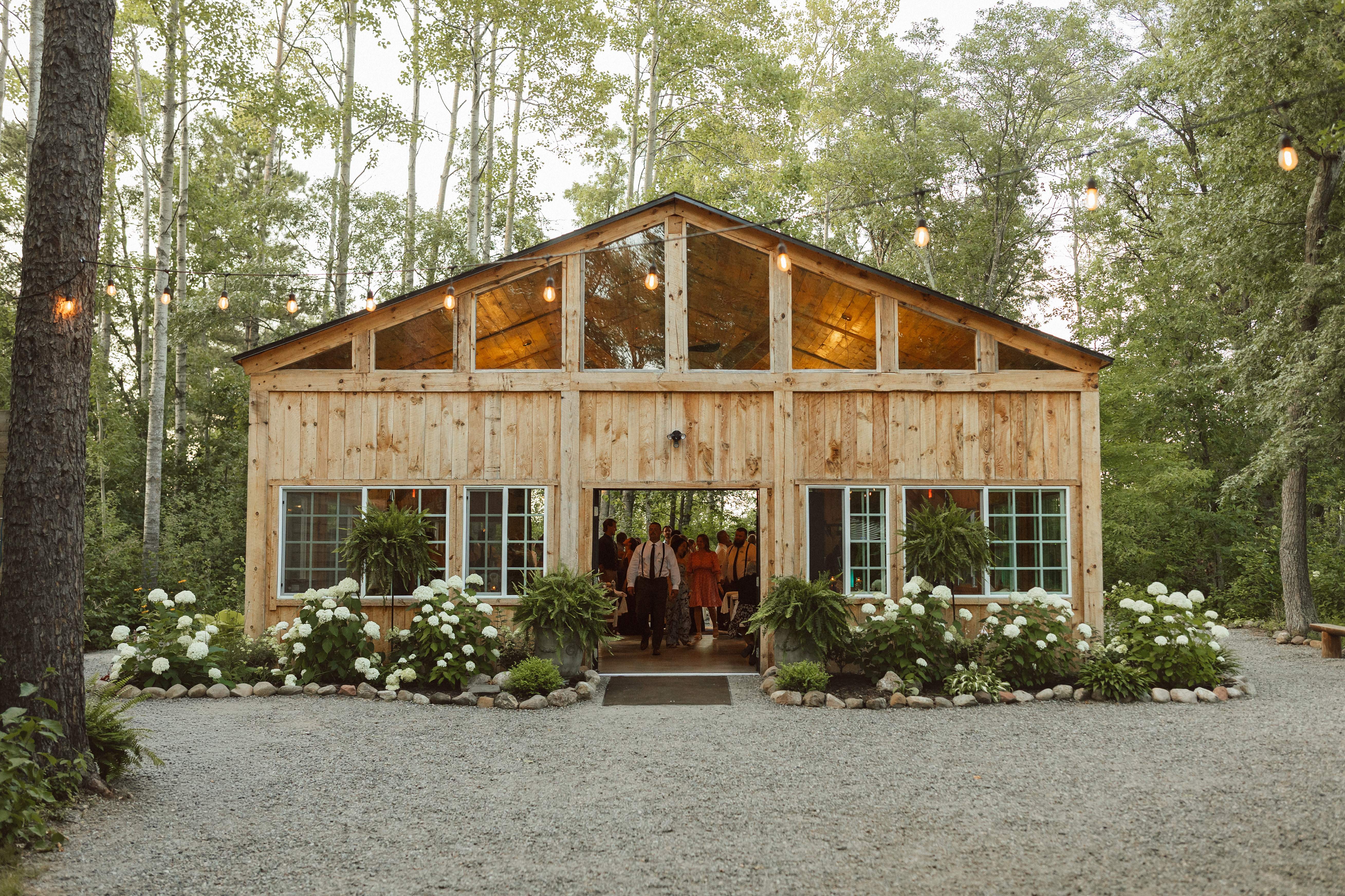 The Emerald Cottage surrounded by woodland, string lights, flowering hydrangeas, and a gravel garden path