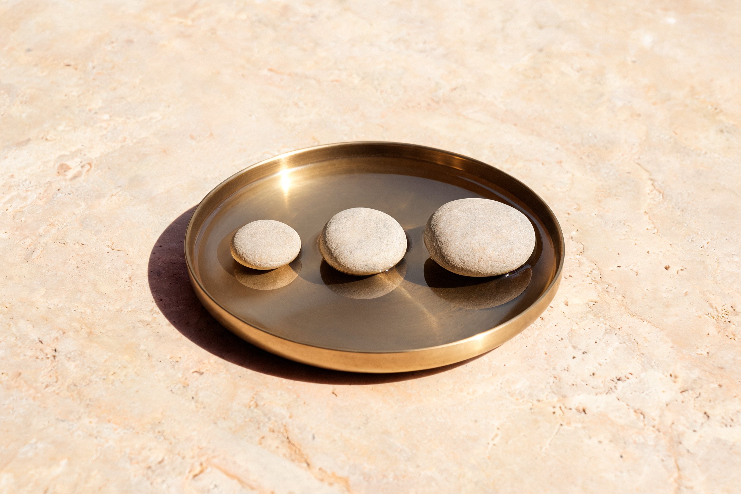 Three smooth stones arranged small to large on a brass tray in warm daylight