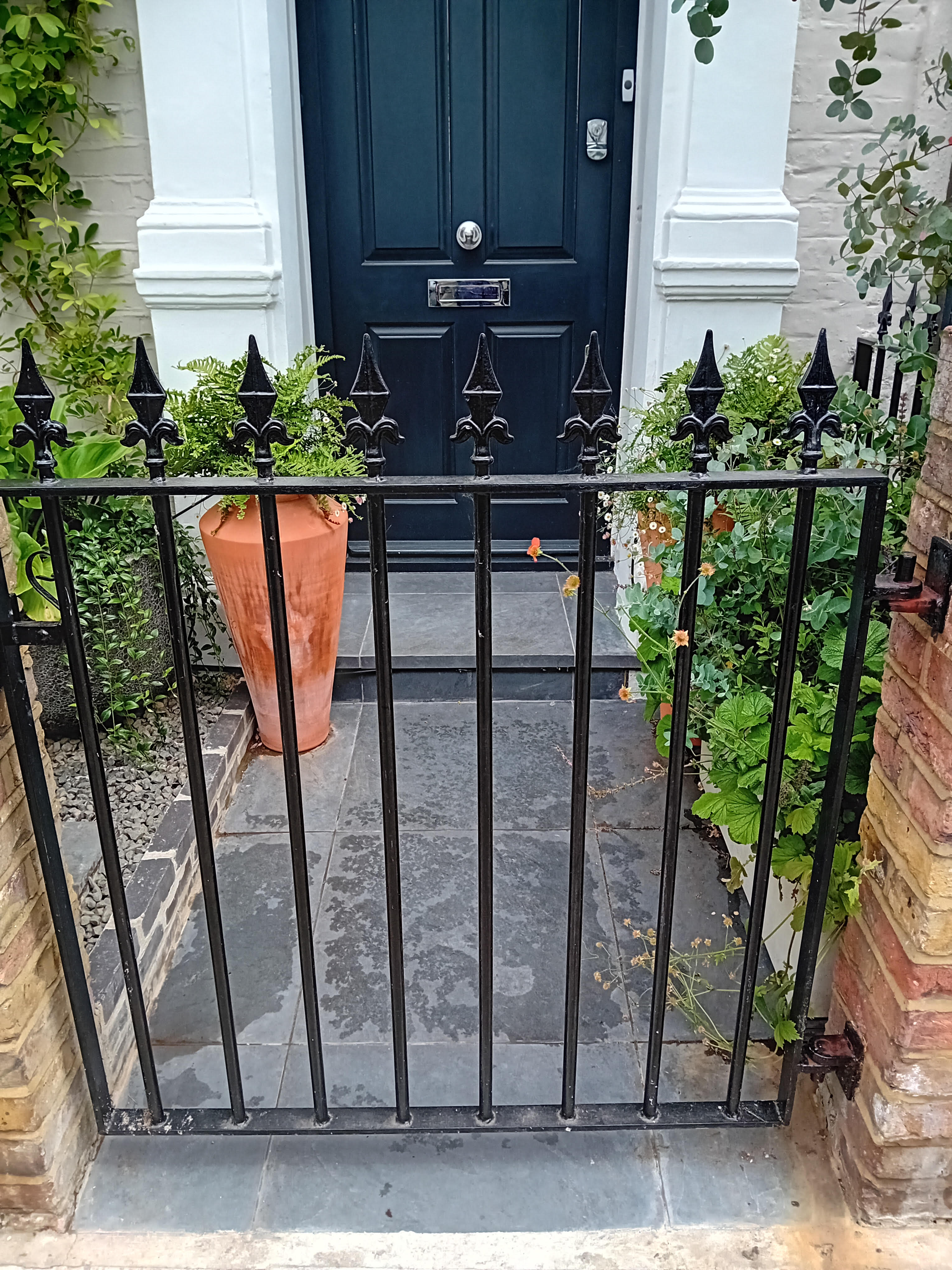 London front garden with black wrought-iron railings and gate, slate paving and a terracotta urn