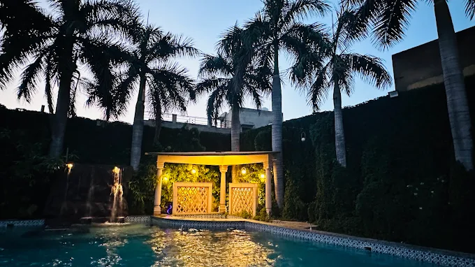 Illuminated poolside pavilion framed by palm trees at dusk