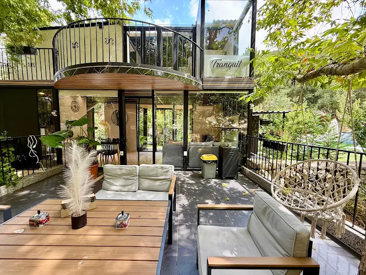 Tranquil Experience outdoor terrace with comfortable seating, macrame chair, and modern glass architecture surrounded by forest