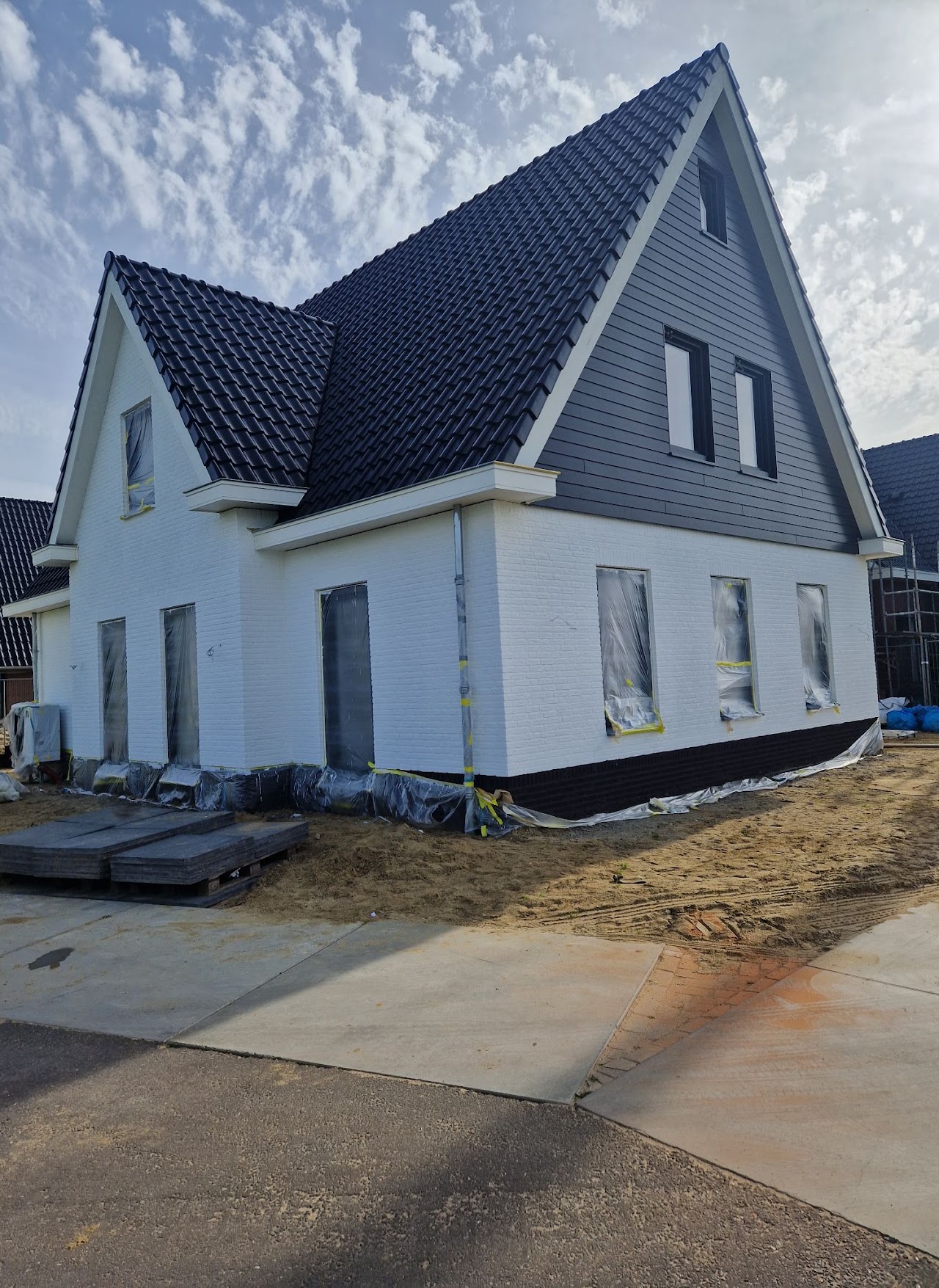 Nieuwbouwwoning met witte gevel, donkere dakpannen en met folie afgeschermde kozijnen