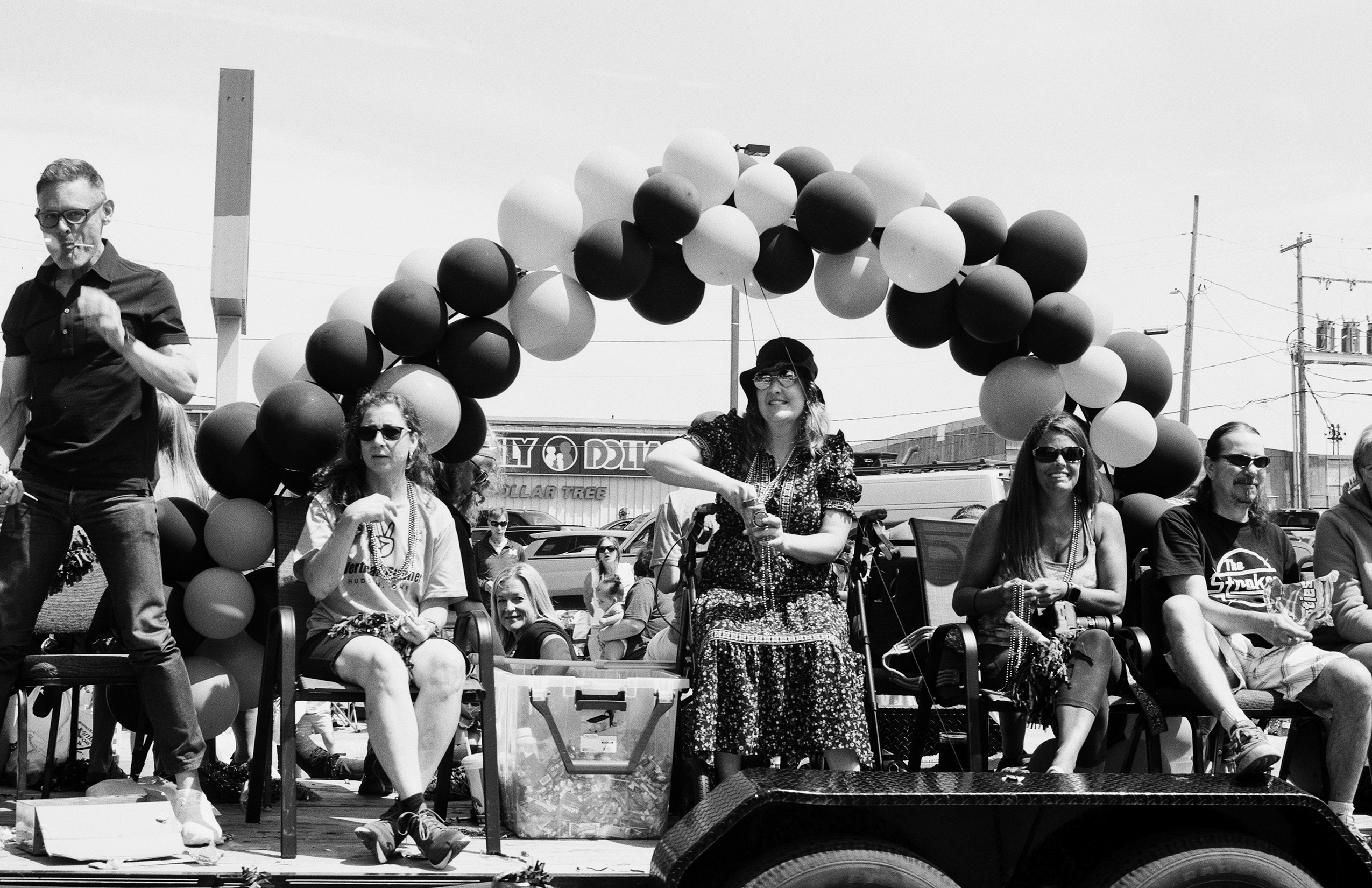 Street parade with crowd and black and white balloons overhead creating festive atmosphere