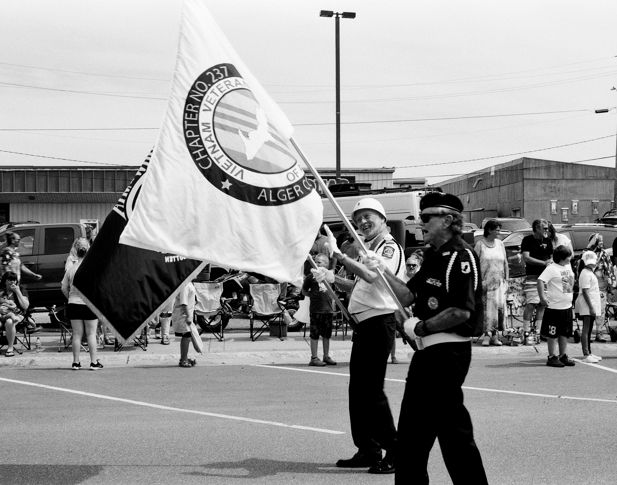American Legion Auxiliary members in white uniforms marching with flag in parade