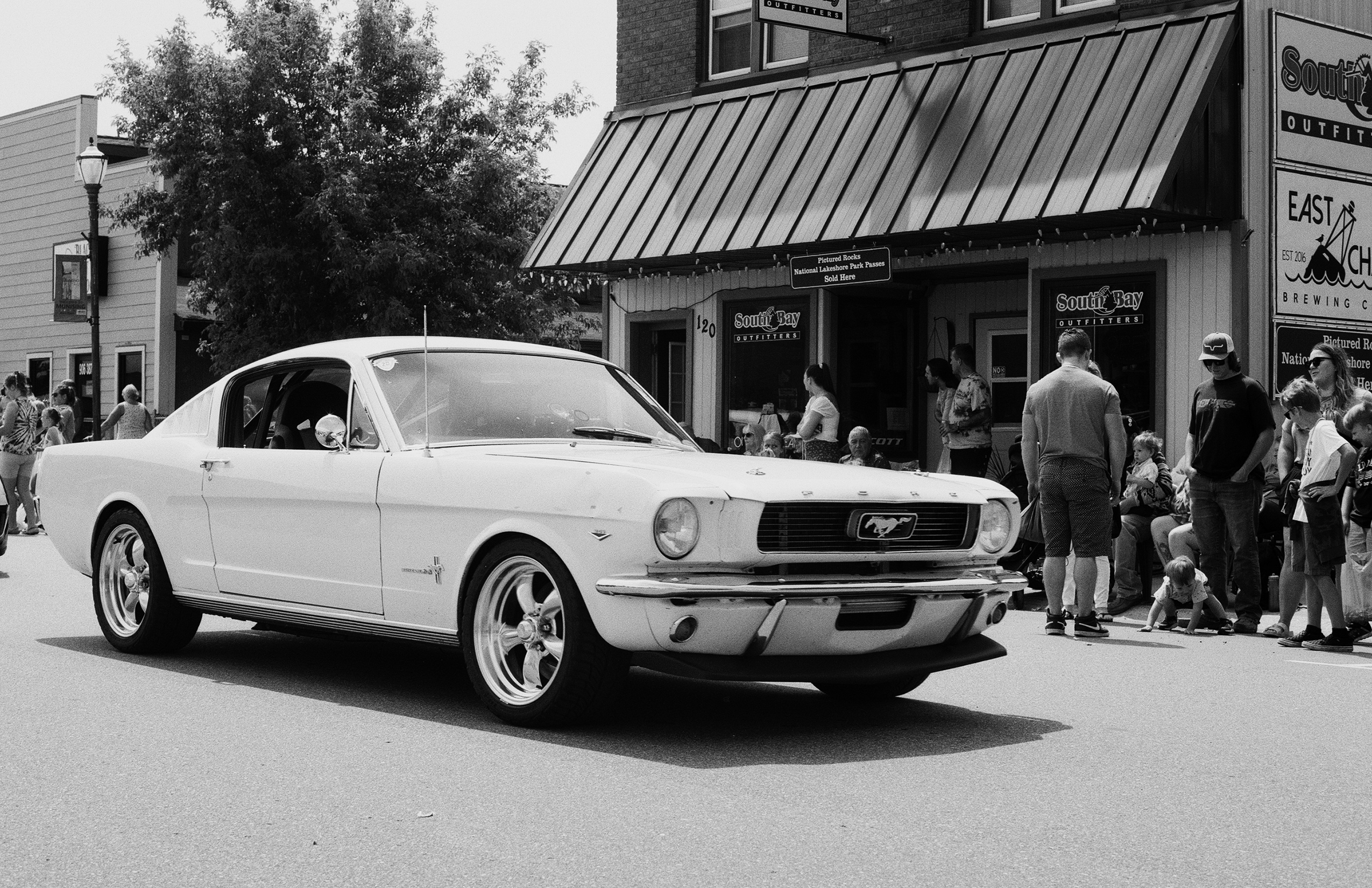 White Mustang classic car on parade street with spectators and storefronts