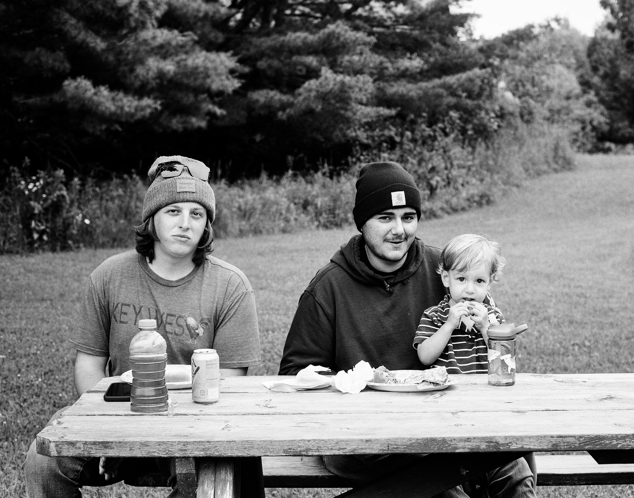 Family of three enjoying picnic lunch at outdoor table with beverages and food