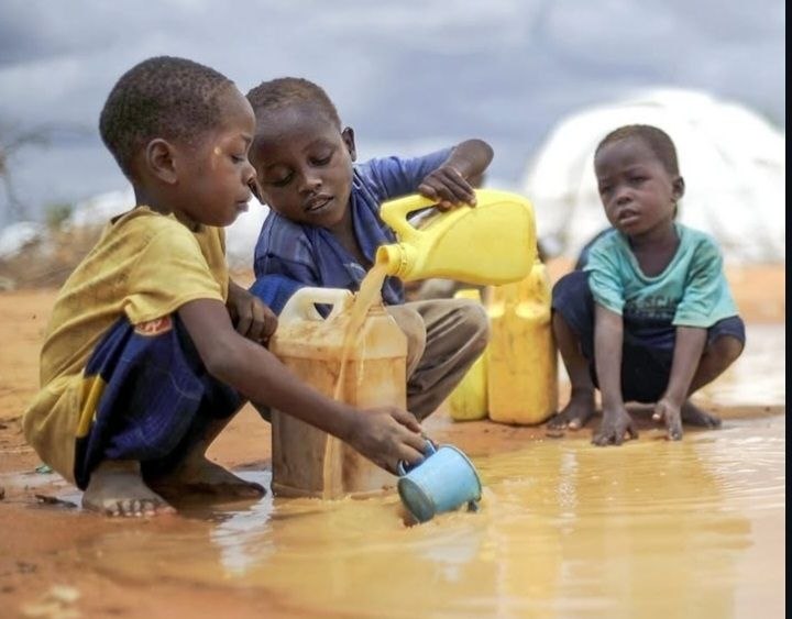 Children collecting water from muddy floodwater while carrying yellow jerry cans