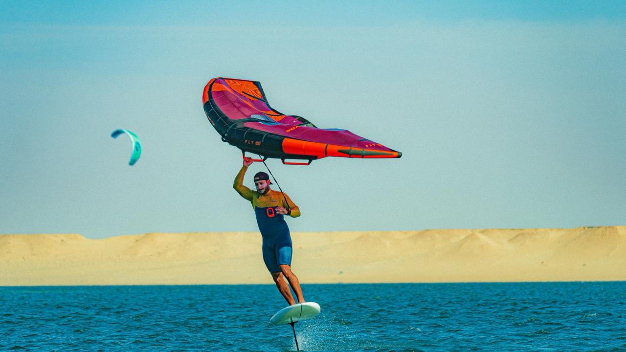 Wingfoiler riding on Dakhla lagoon with FLY wing, desert dunes in background