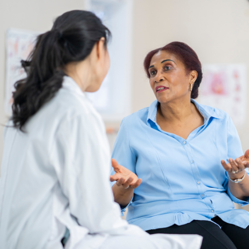 A woman in a blue blouse gesturing as she speaks openly with a healthcare provider in a white coat